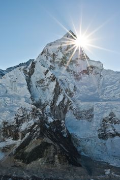 the sun shines brightly on top of a snowy mountain peak, with snow - capped mountains in the foreground