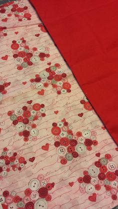 a red table cloth with buttons and hearts on it, next to a pair of scissors