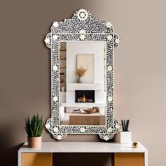 a mirror sitting on top of a white table next to a potted plant in front of a fireplace