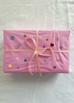 a pink wrapped gift box with bows and confetti on the top, sitting on a white sheet