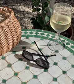 a glass of wine sitting on top of a table next to a basket and sunglasses