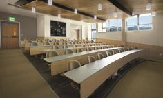 an empty lecture hall with rows of desks and chairs in front of large windows