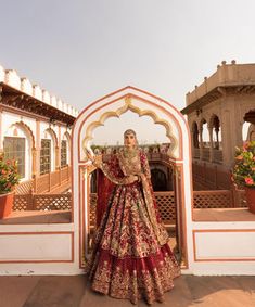 a woman in a red and gold bridal gown standing on a balcony with potted plants