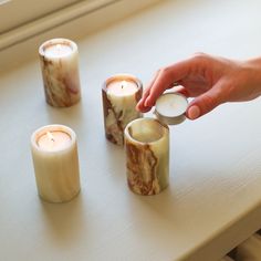 a person lighting candles on a table with other items around it and another candle in the foreground