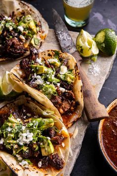 three tacos with meat, lettuce and cheese on them next to a bowl of salsa