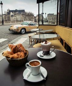 two cups of coffee sit on a table with pastries and croissants