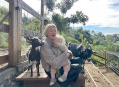 a woman holding a baby while sitting on a bench next to two goats and another goat