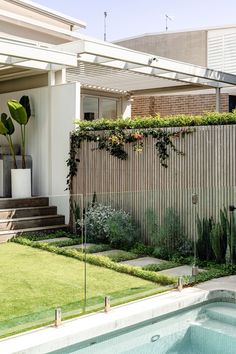 an outdoor swimming pool in front of a house with a wooden fence and green grass