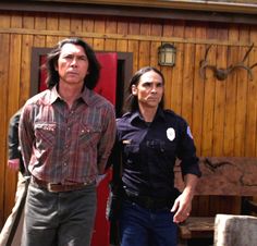 two people standing next to each other in front of a wooden building with antlers on the wall