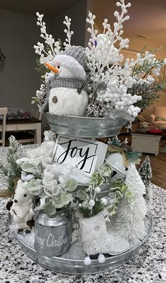 a snowman in a bucket filled with white flowers and other holiday decorations on top of a table