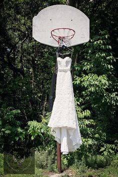 a wedding dress hanging from a basketball hoop in the woods with trees behind it,