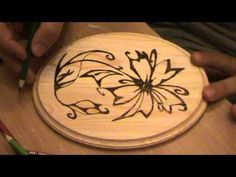 someone is drawing on a wooden plate with black ink