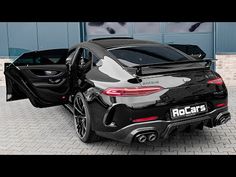 the rear end of a black sports car parked in front of a building with its door open