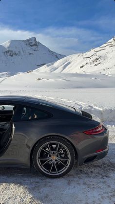 a grey sports car parked in the snow with its door open and mountains in the background