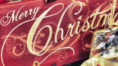 a merry christmas sign hanging from the side of a red box with gold lettering on it