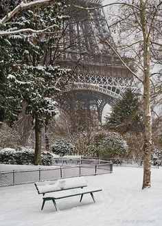 a park bench covered in snow next to the eiffel tower