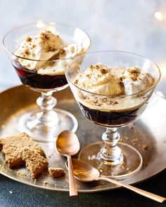 two glasses filled with ice cream and dessert on top of a metal tray next to spoons