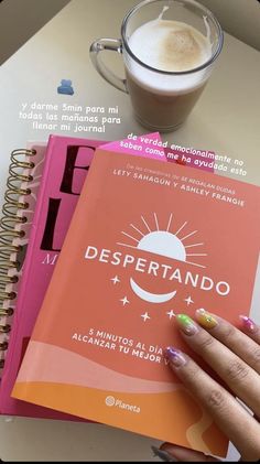 a woman's hand holding a book next to a cup of coffee