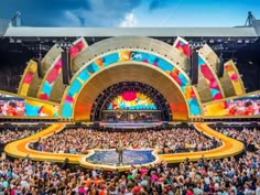 an outdoor concert venue with lots of people sitting on the stage and in front of it