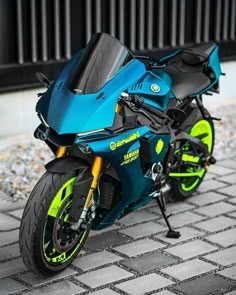 a blue and yellow motorcycle parked on top of a brick floor next to a building