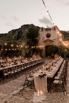 an outdoor dining area with long tables and candles lit up at the end of each table