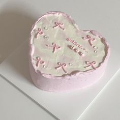 a heart shaped cake with pink bows on it sitting on a white table top next to a knife