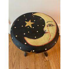 a wooden stool with a painted moon and star on it's face, sitting on a wood floor