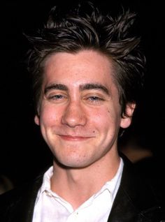 a close up of a person wearing a suit and smiling at the camera with his hair blowing in the wind