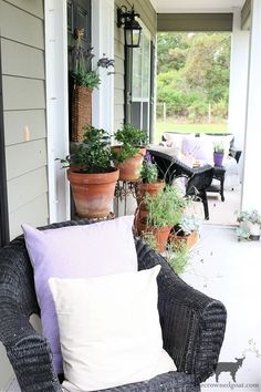 the front porch is decorated with potted plants and wicker furniture, along with pillows