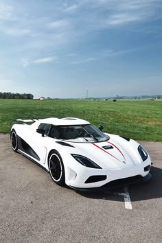 a white sports car parked in a parking lot next to an open field with green grass