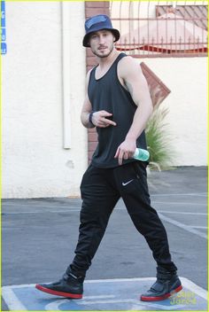 a man walking across a parking lot wearing a hat