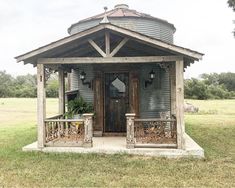 a small wooden building with a metal roof and porch on the grass near some trees