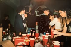 a group of young people standing around a table full of drinks and sodas,