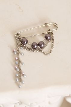 a close up of a brooch pin with pearls and chains on it's side