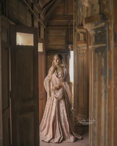 a woman is standing in an open doorway wearing a pink and gold wedding dress with her hands on her head