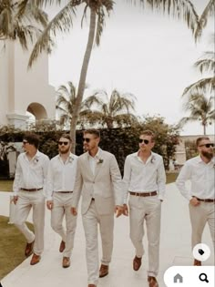 a group of men in white suits and sunglasses walking down a sidewalk next to palm trees