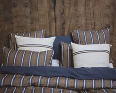 a bed with blue and white striped pillows on it's headboard next to a wooden wall