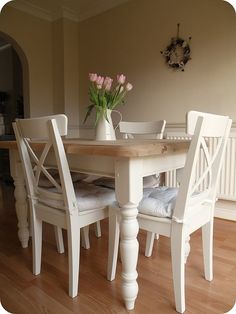 a white table with four chairs and a vase filled with flowers on top of it