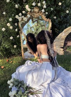 two women sitting in front of a mirror with angel wings on their backs and one holding a flower