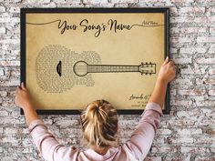 a woman holding up a guitar poster with the words your song's name