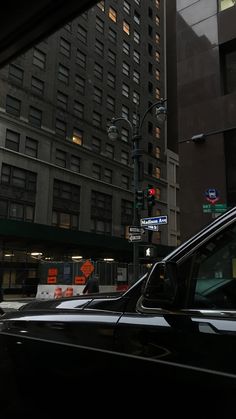 a black car driving down a city street next to tall buildings and traffic lights at night