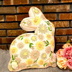 a stuffed rabbit sitting next to flowers on top of a fur covered floor in front of a brick wall