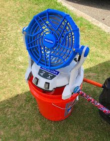 a blue and white fan sitting on top of a red trash can in the grass