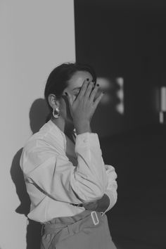 black and white photograph of a woman covering her face with both hands while standing in front of a wall