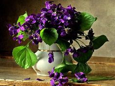 a white vase filled with purple flowers on top of a wooden table