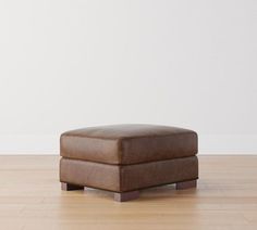 a brown ottoman sitting on top of a hard wood floor next to a white wall