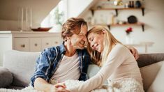 a man and woman sitting on top of a couch next to each other in a living room