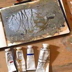 three tubes of paint sitting on top of a wooden table next to a painting board