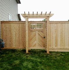 a wooden gate in the grass next to a fence with a trellis on it