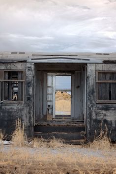 an old run down train car sitting in the middle of a dry grass field with broken windows